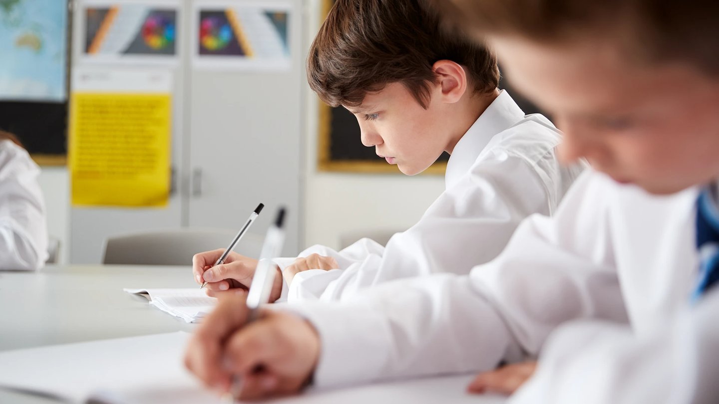 Students Wearing Uniform Sitting And Working Around Table In Lesson